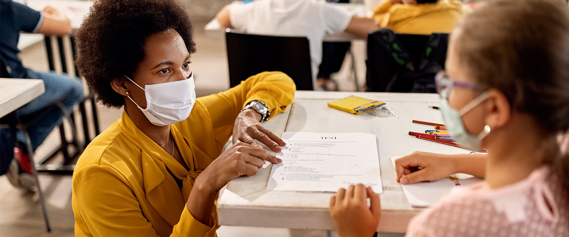 An African American teacher and a schoolgirl wear protective face masks while discussing test results in a New Mexico classroom.