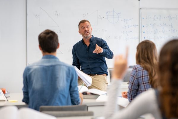 Professor pointing at college student with hand raised in classroom. Student raising a hand with a question for the teacher. Lecturer teaching in class while girl have a question to do during a lesson