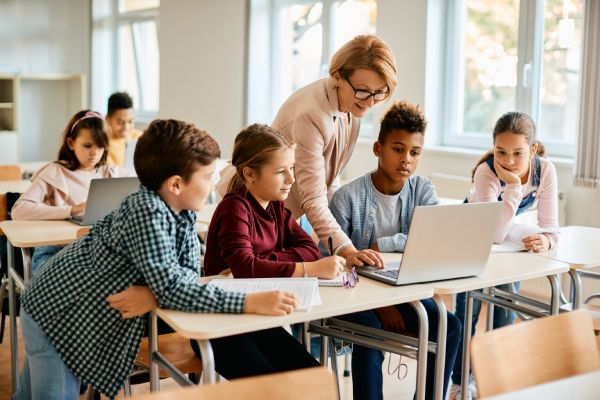 Una profesora de primaria y sus alumnos utilizan un portátil durante una clase de informática en el colegio.