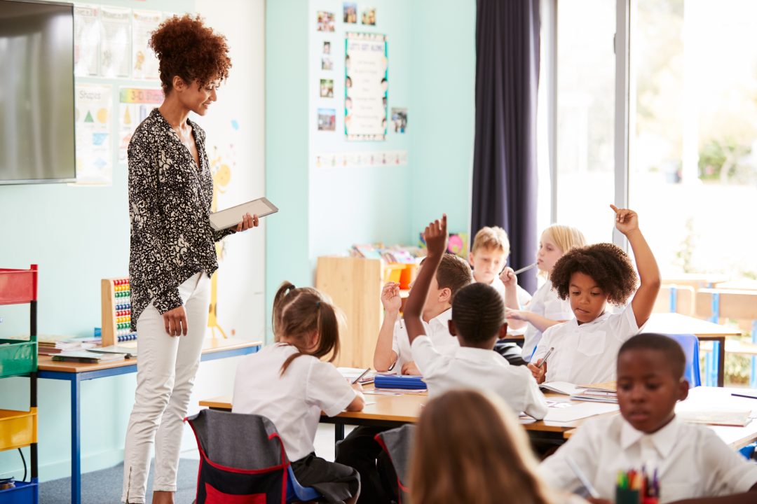 Una profesora con una tableta digital enseña a un grupo de alumnos uniformados de primaria en el aula de un colegio