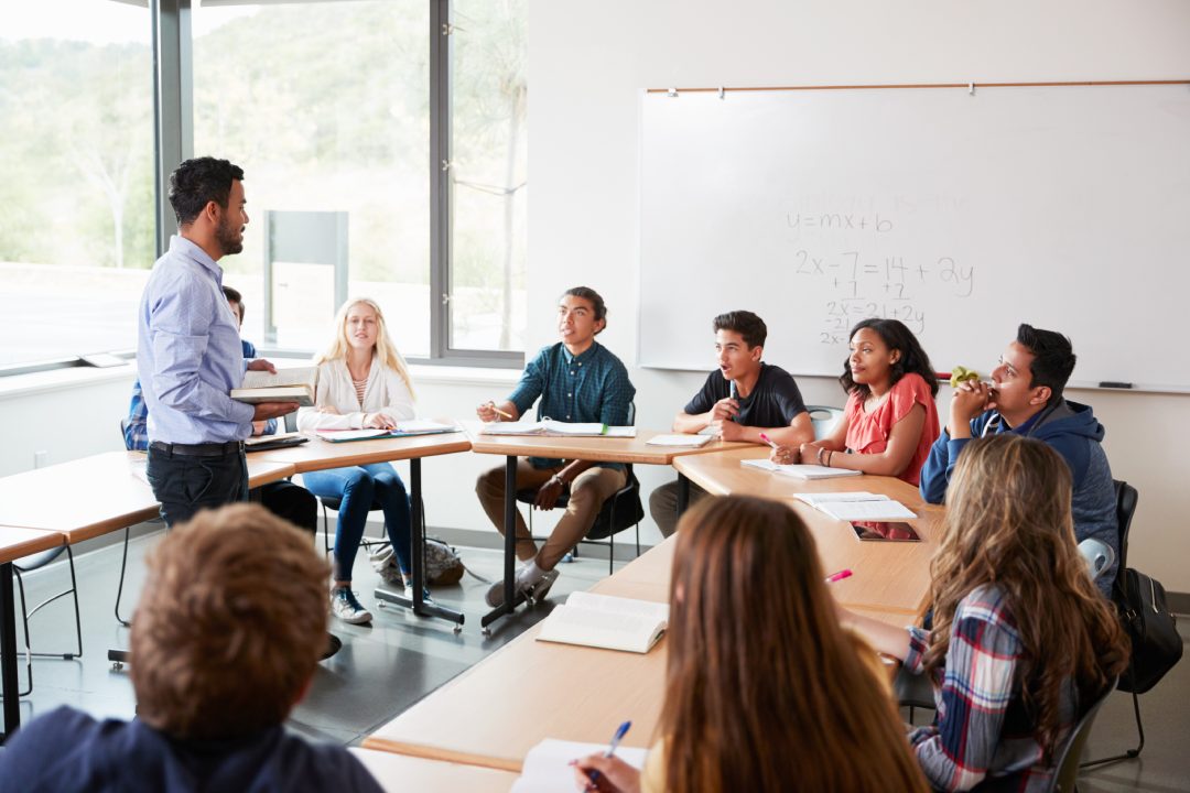 Male High School Tutor With Pupils Sitting At Table Teaching Maths Class