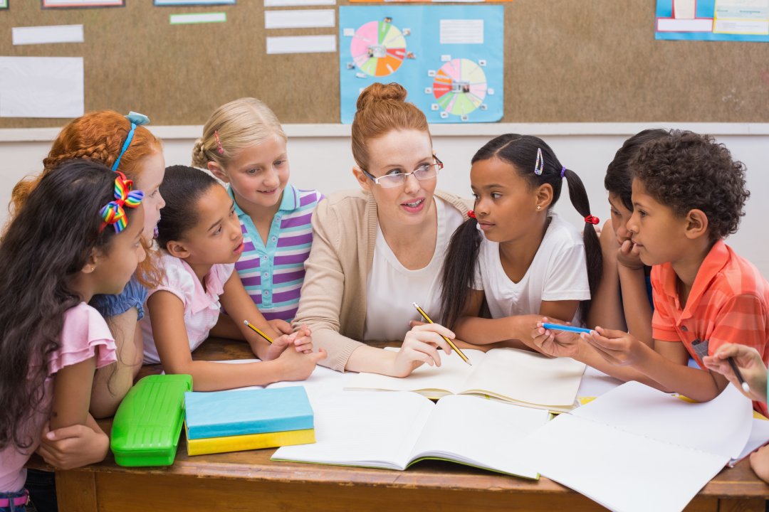 Profesor y alumnos trabajando juntos en el pupitre de la escuela primaria