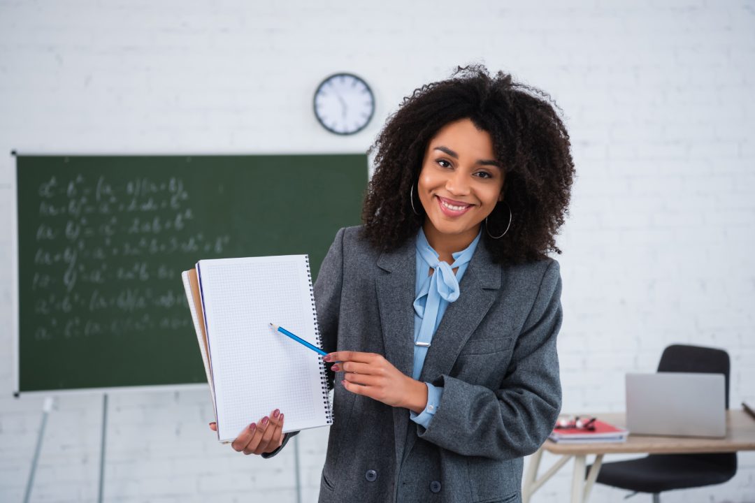 Smiling african american teacher pointing at notebook in classroom