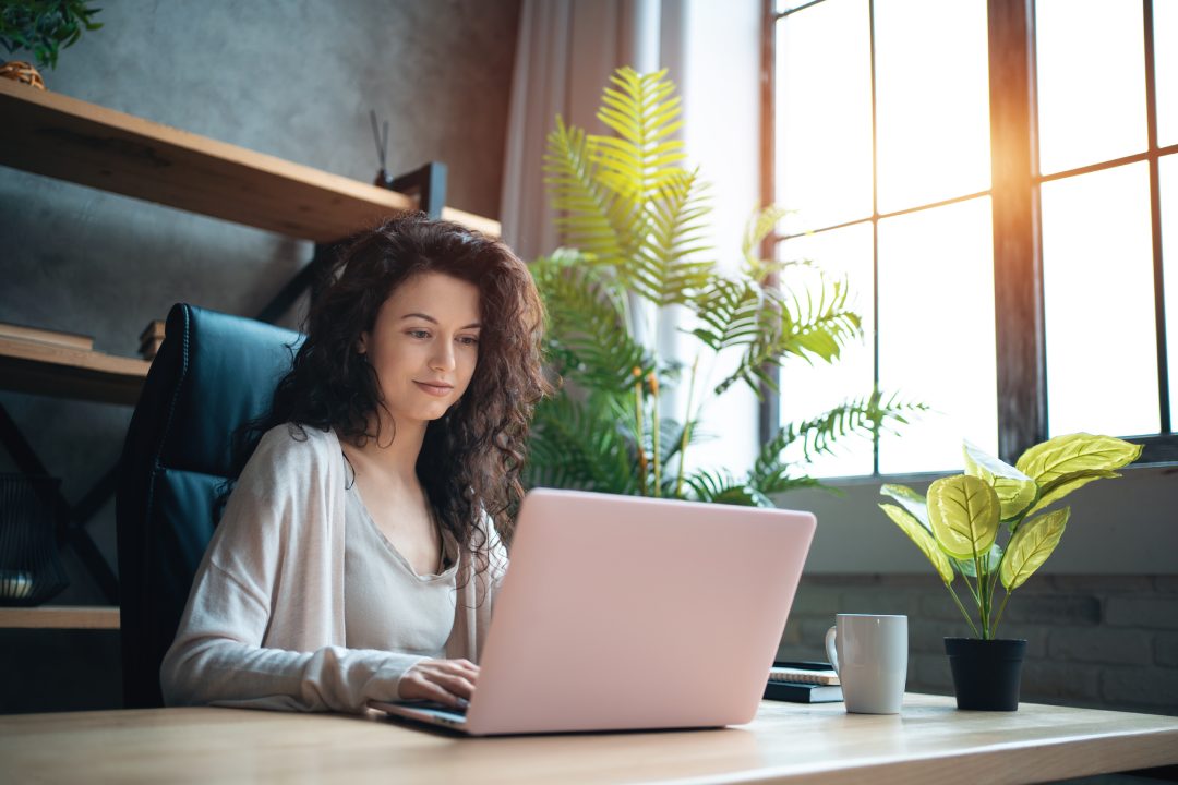 cheerful female manager working with laptop and typing at home office