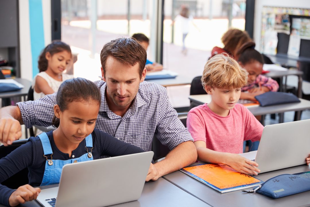 Teacher helping young students using laptops in class