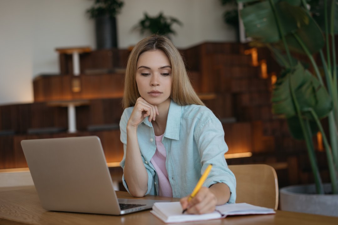 Pensive businesswoman using laptop computer, taking notes, working project. Student studying, distance learning, exam preparation, education concept