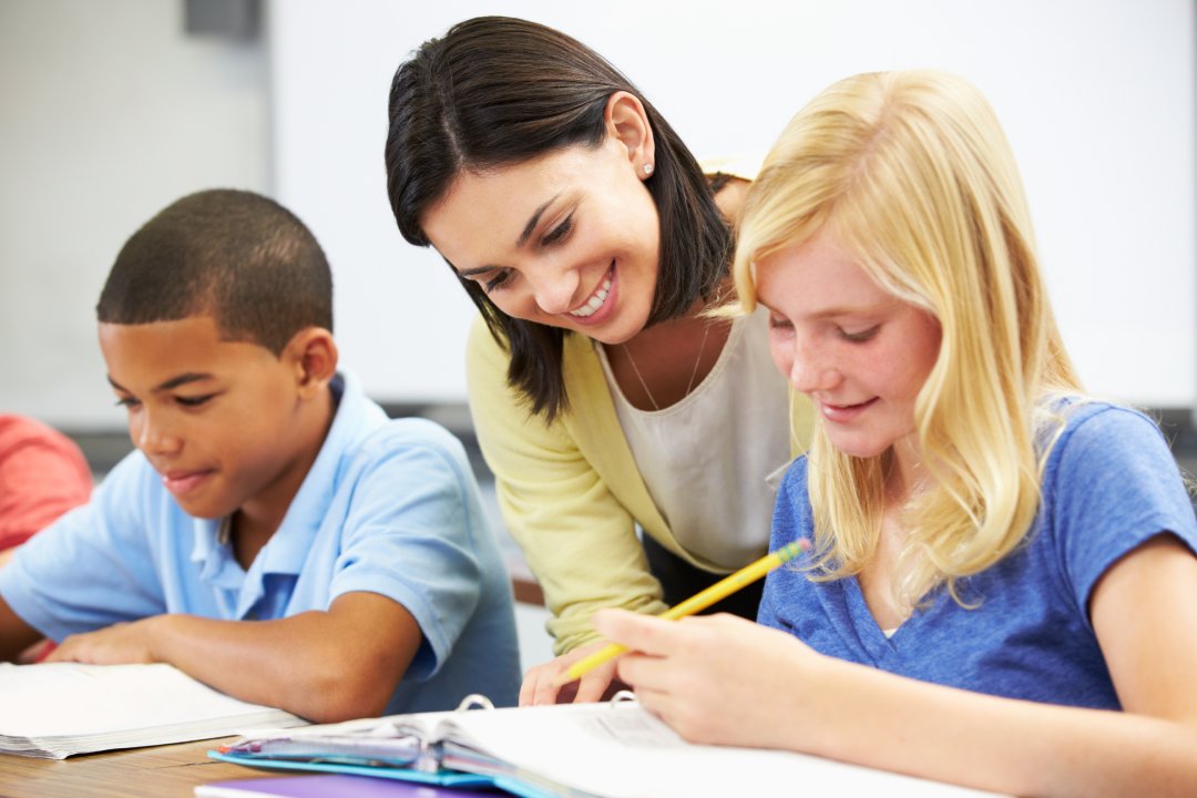 Teacher Helping Pupils Studying At Desks In Classroom