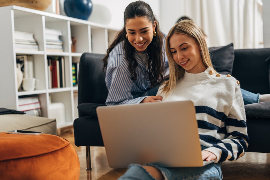 Dos hermosas mujeres jóvenes están utilizando portátil juntos