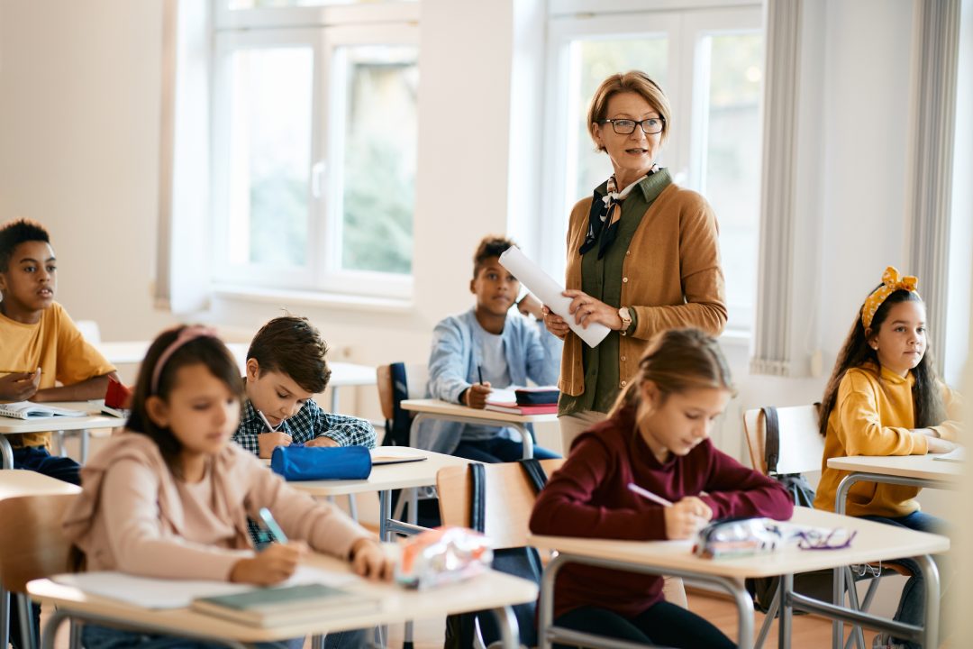 Mature teacher holding a class to group of school kids at primary school.