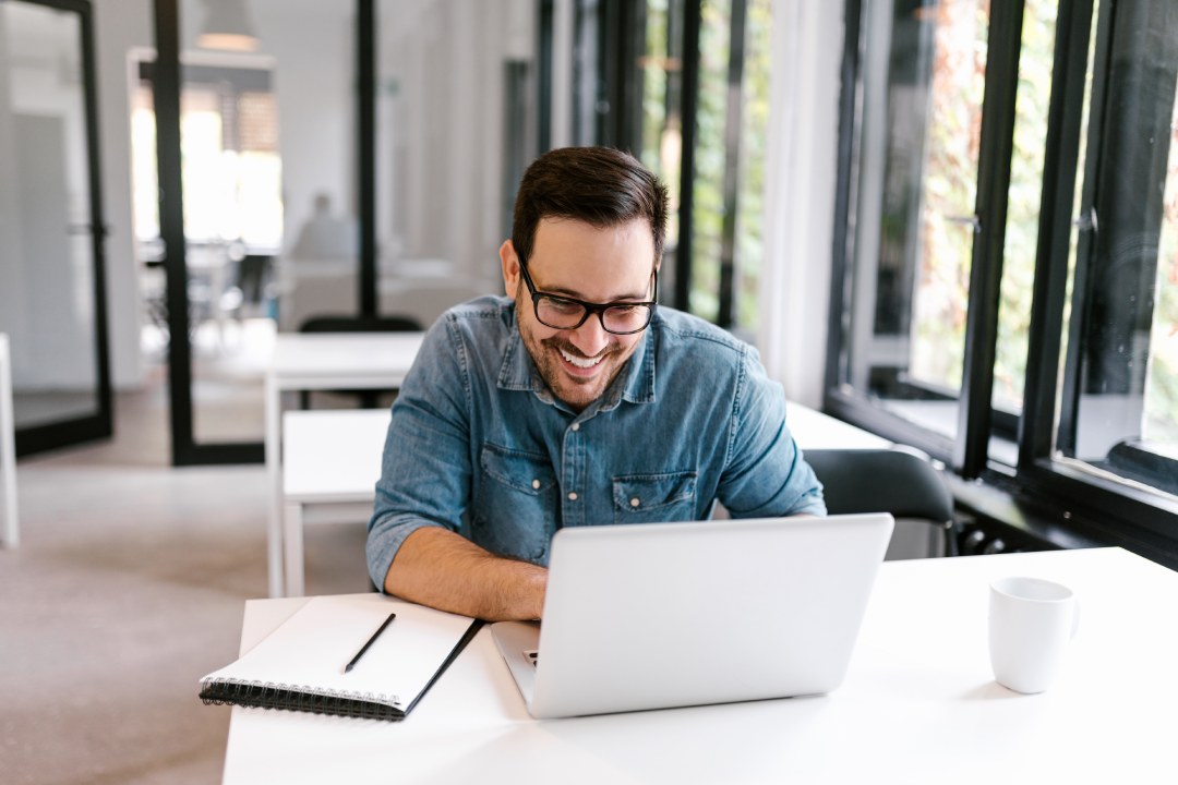 Cheerful businessman using laptop in bright office space.