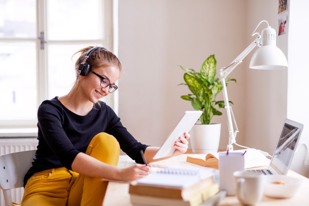 Una joven estudiante sentada a la mesa, utilizando una tableta para estudiar.