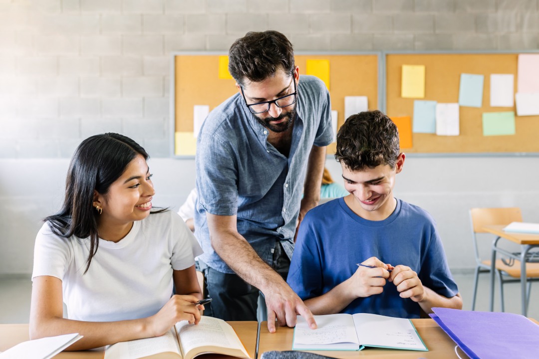 Profesor masculino ayudando a estudiantes de secundaria a hacer ejercicios en clase - Concepto de educación y gente universitaria