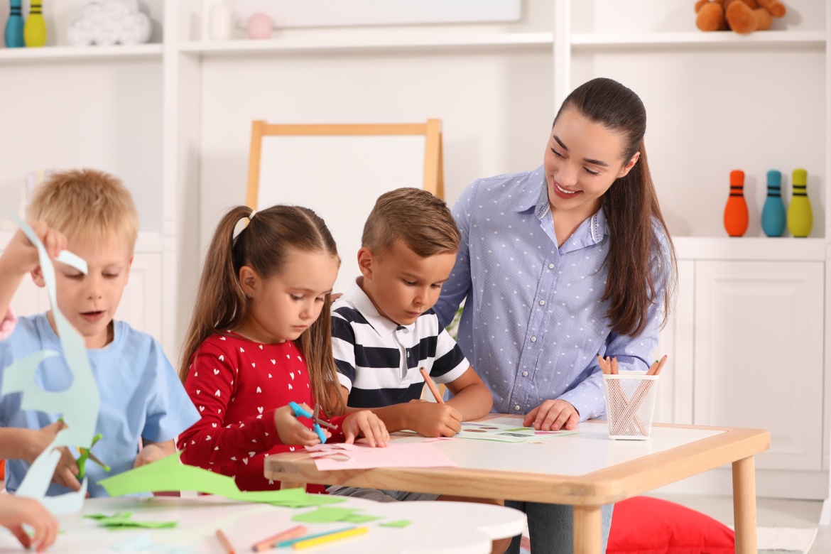 Maestra de guardería y un grupo de simpáticos niños jugando en los pupitres de una guardería. Actividades lúdicas