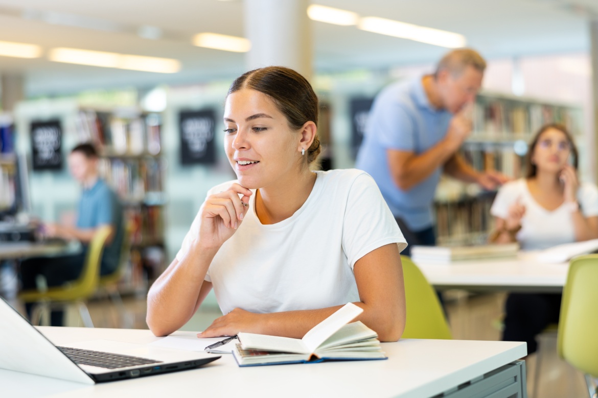 Chica caucásica estudiante de colegio investigando en el portátil del proyecto en la biblioteca del colegio