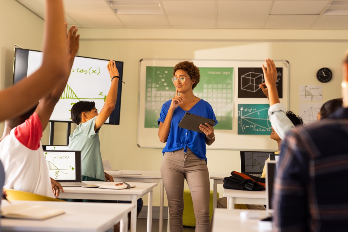 En el instituto, un profesor sostiene una tableta y hace participar a los alumnos que levantan la mano en clase. Educación, enseñanza, aprendizaje, tecnología, compromiso, interacción