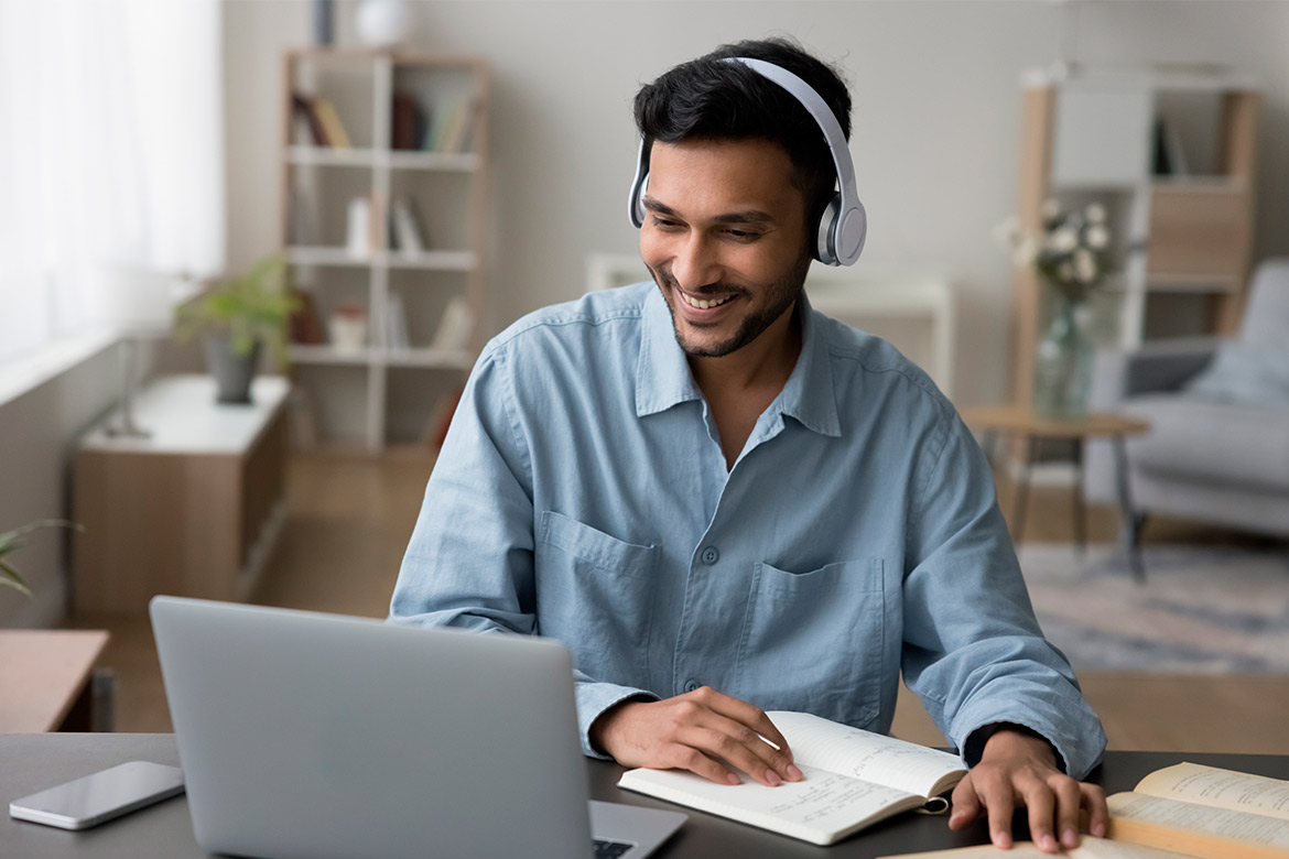 man studying in front of laptop with headphones and notebook 