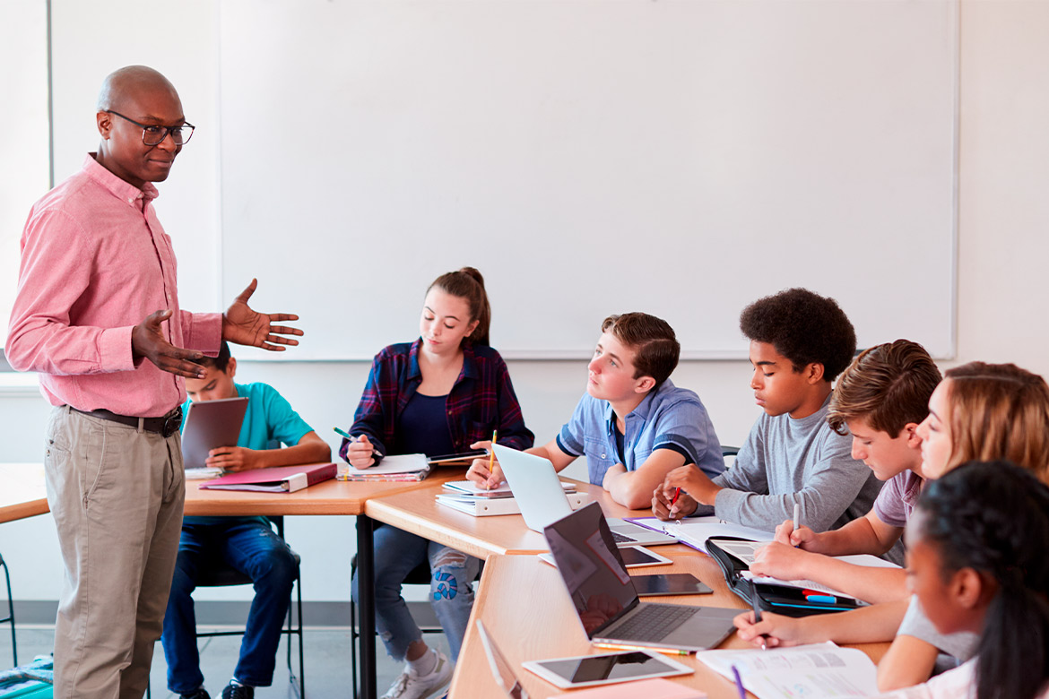 man teacher speaking with young students in a classroom