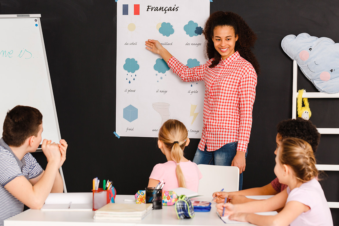 A woman instructs children about weather concepts in a classroom setting, engaging them with interactive materials.