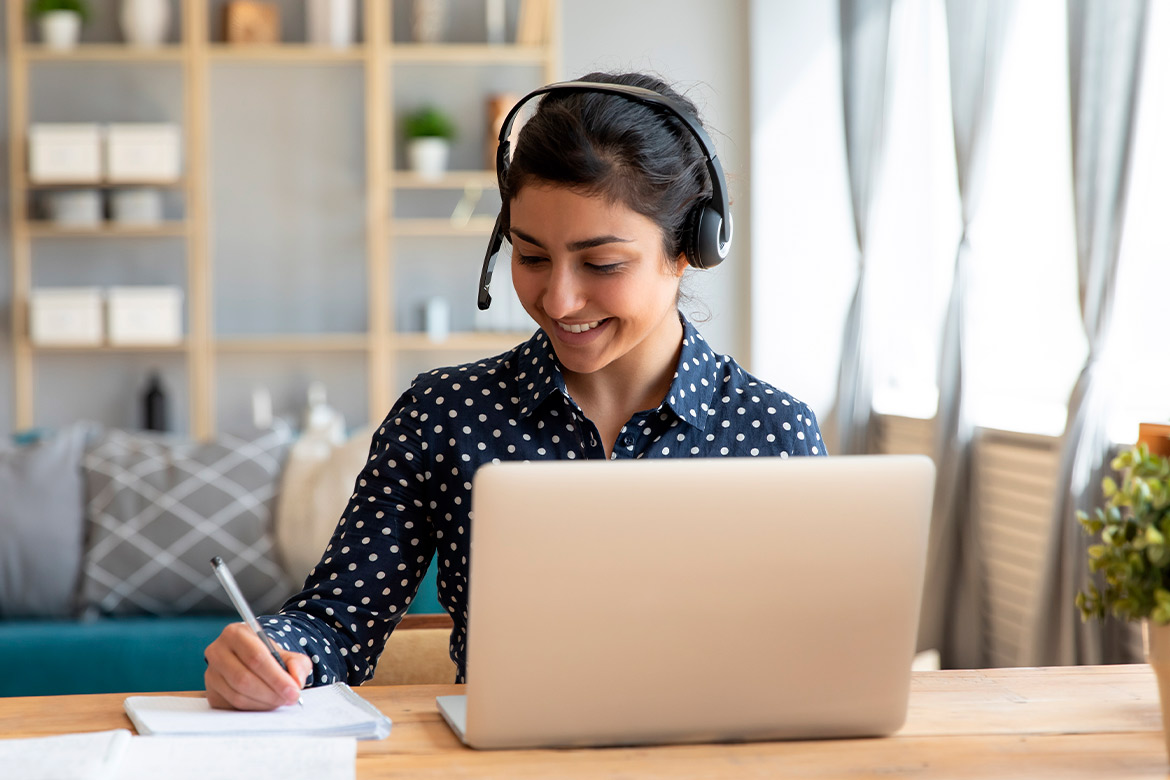 A woman with a headset sits at a desk with a laptop, focused on teaching from Texas while based in Spain.