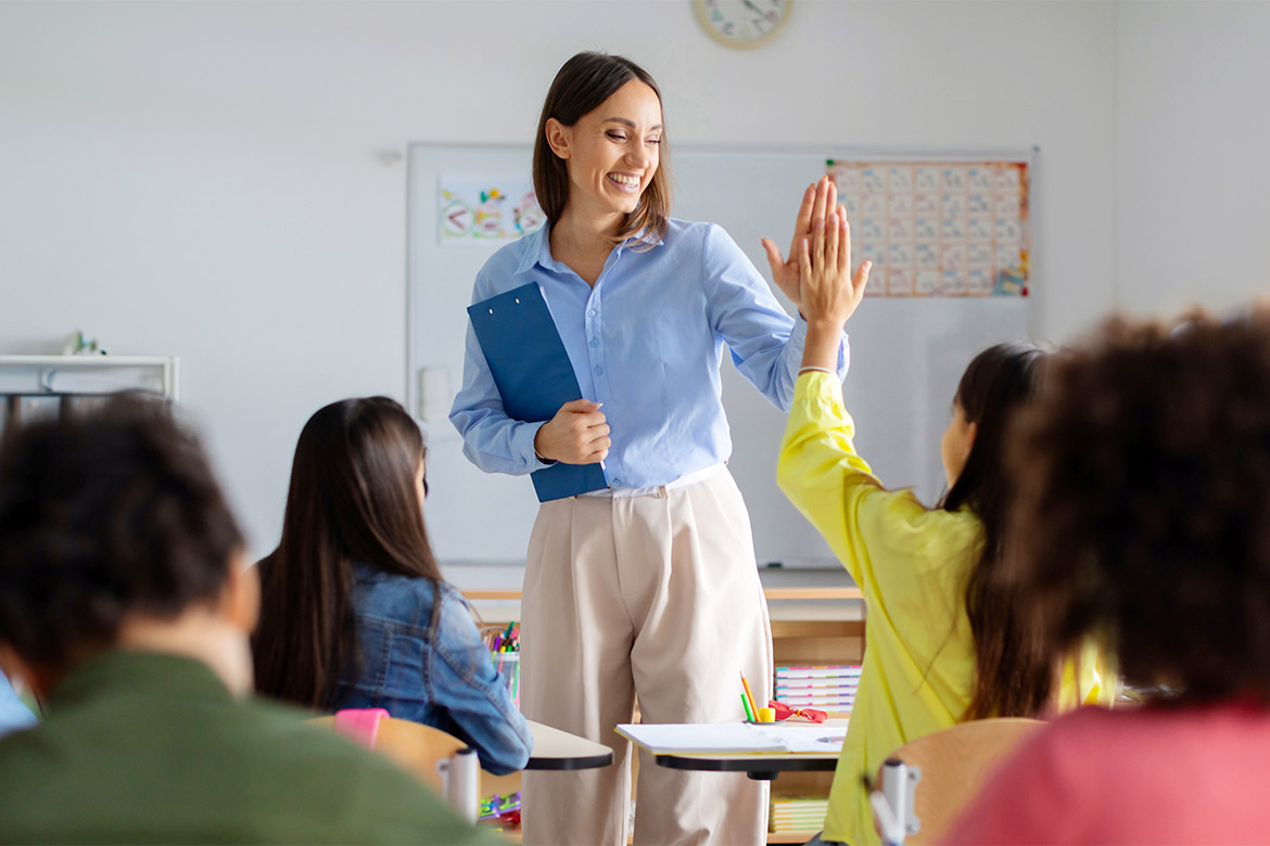A teacher joyfully high-fives her students in a classroom, celebrating their achievements together.
