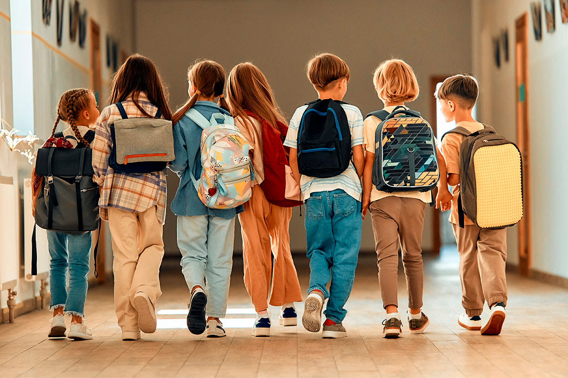 Several children carrying backpacks stroll through a brightly lit hallway, chatting and enjoying their time together.