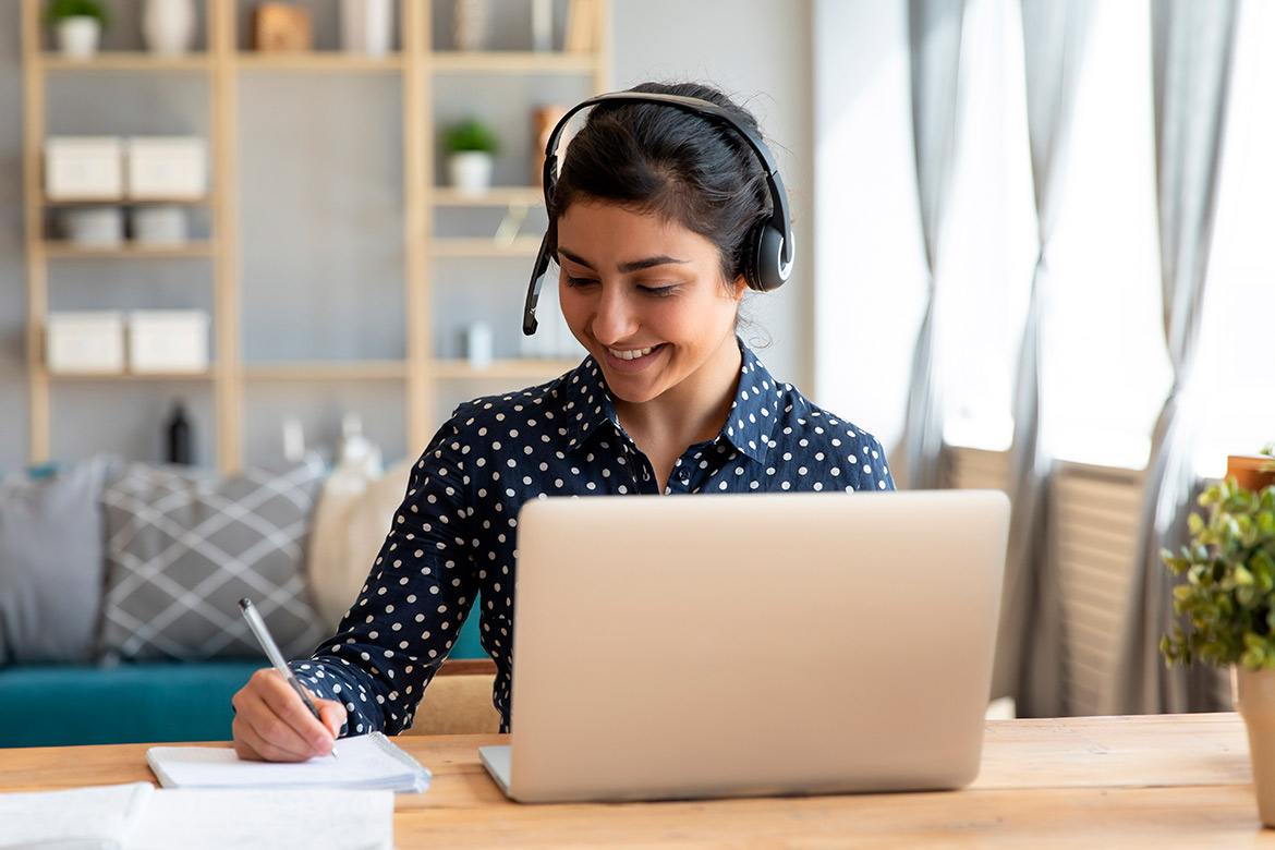 A woman wearing a headset works at her desk with a laptop, researching steps to become a teacher in Laredo.