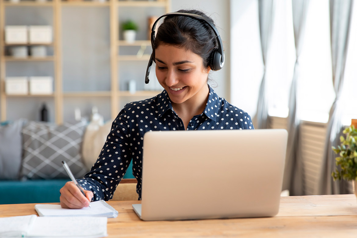 A woman wearing a headset works at her desk with a laptop, researching Virginia certification for teaching in Texas.