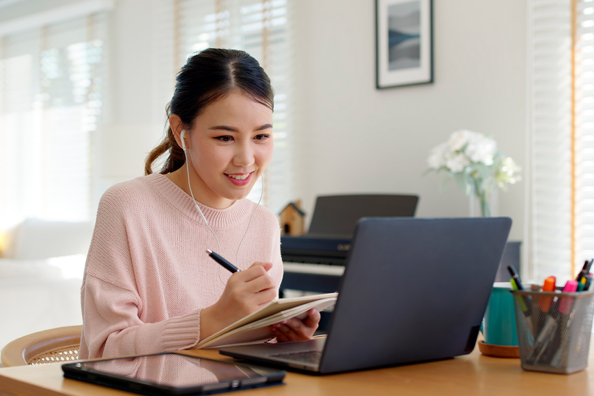 A woman sits at a table with a laptop, focused on her work, possibly researching teaching opportunities in Texas.