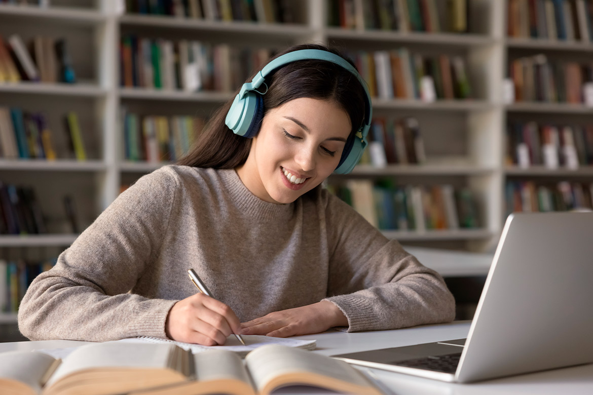 A woman wearing headphones is seated at a table with a laptop, researching pathways to become a Chinese teacher in Texas.