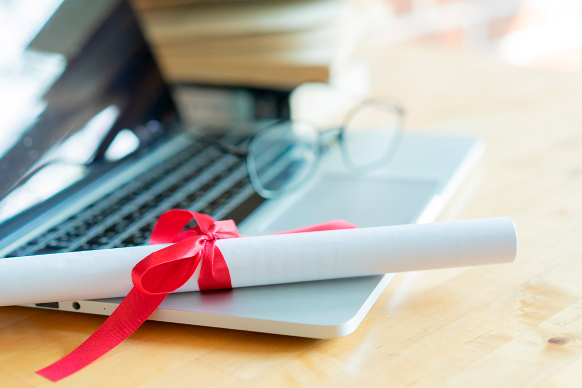 A laptop with a diploma and glasses on a table, representing the journey to becoming a Journalism teacher in Texas.
