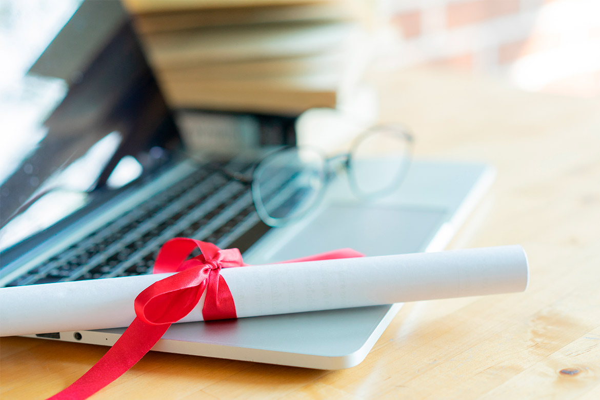 A laptop with a diploma and glasses rests on a table, representing academic achievement and teaching aspirations.