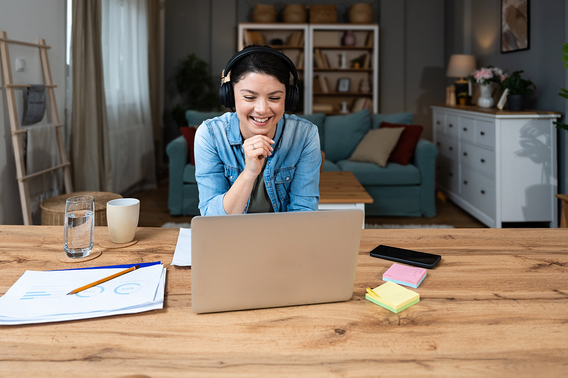 A woman sits at a table with a laptop and a cup of coffee, focused on her work.