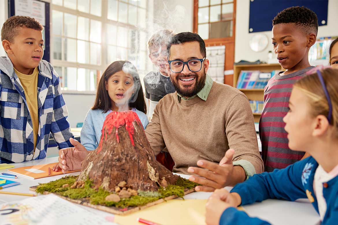 A teacher demonstrates a volcano model to students in a classroom, illustrating geography concepts in Texas education.