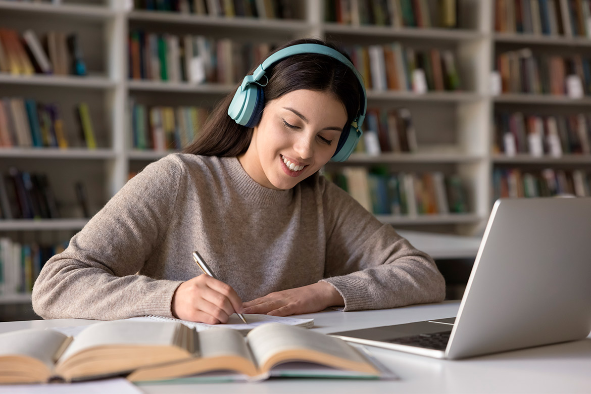 A woman wearing headphones is seated at a table, engaged with her laptop while learning about Texas HB 2 for future teachers.