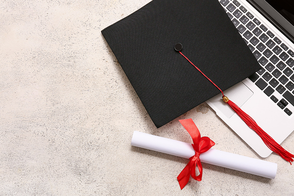 Graduation cap, laptop, and diploma resting on concrete, symbolizing achievement and education in a modern setting.