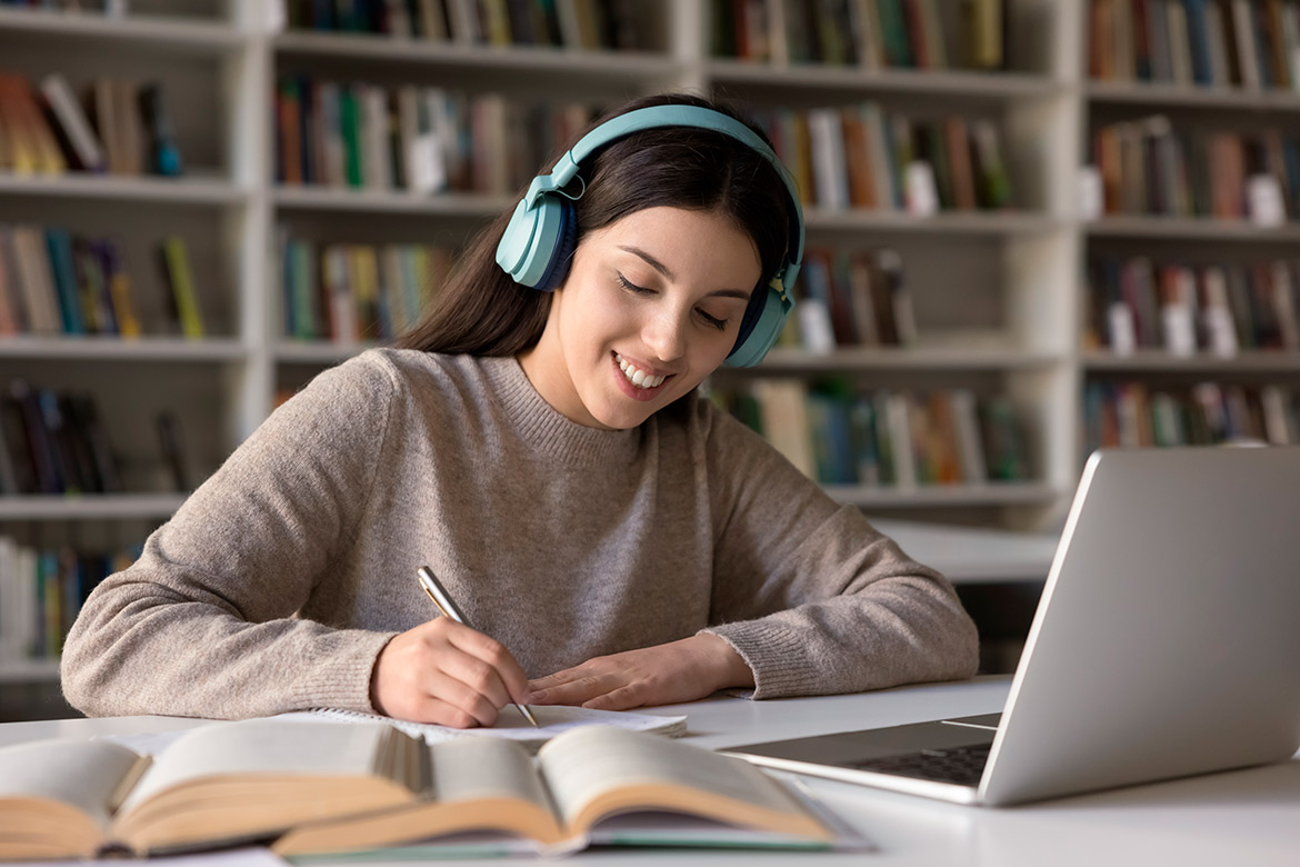 A woman wearing headphones is seated at a table, engaged with her laptop, representing a productive work setting.