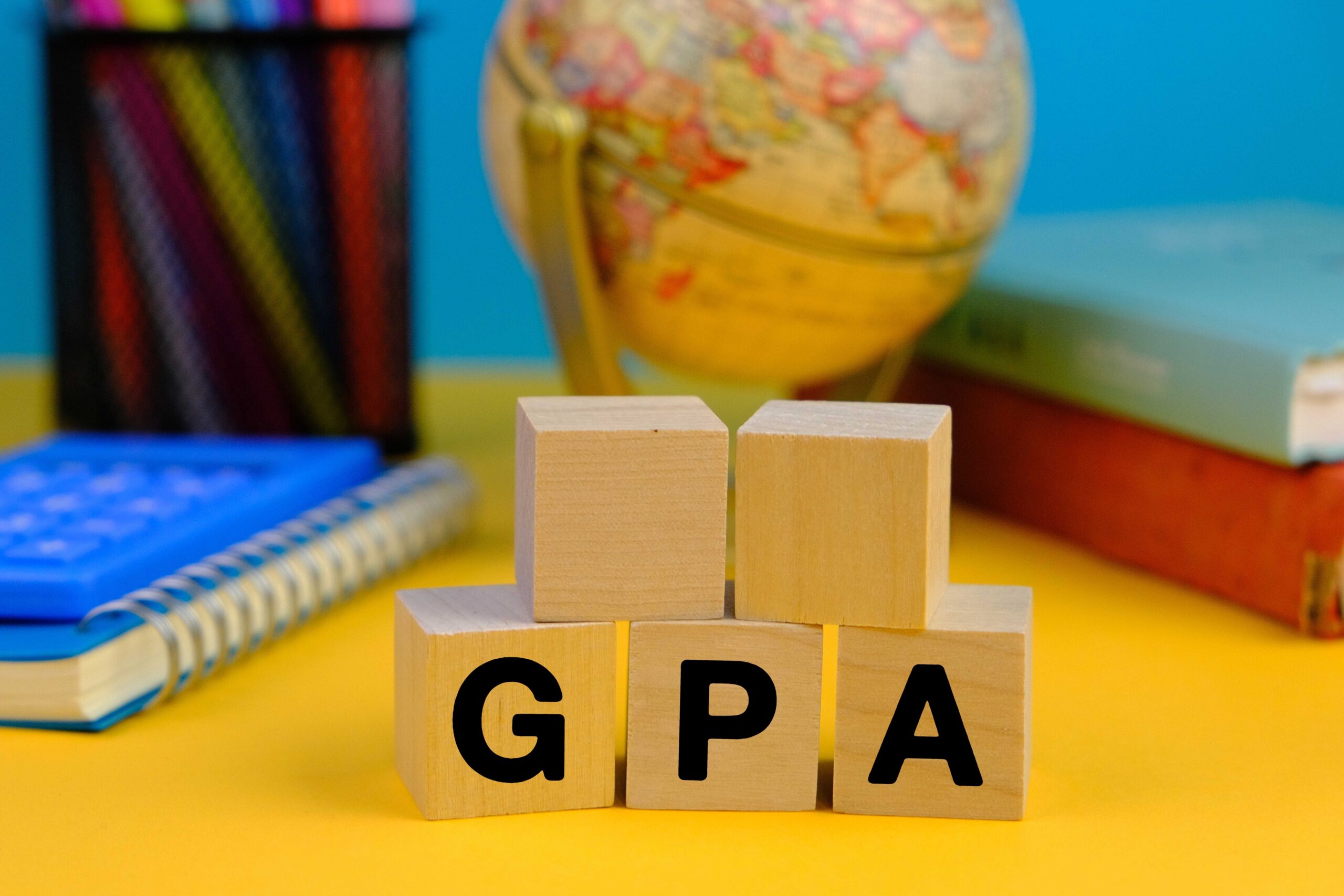 wooden block with the letters GPA or the word grade point average with the background of office tools, blue and yellow background.