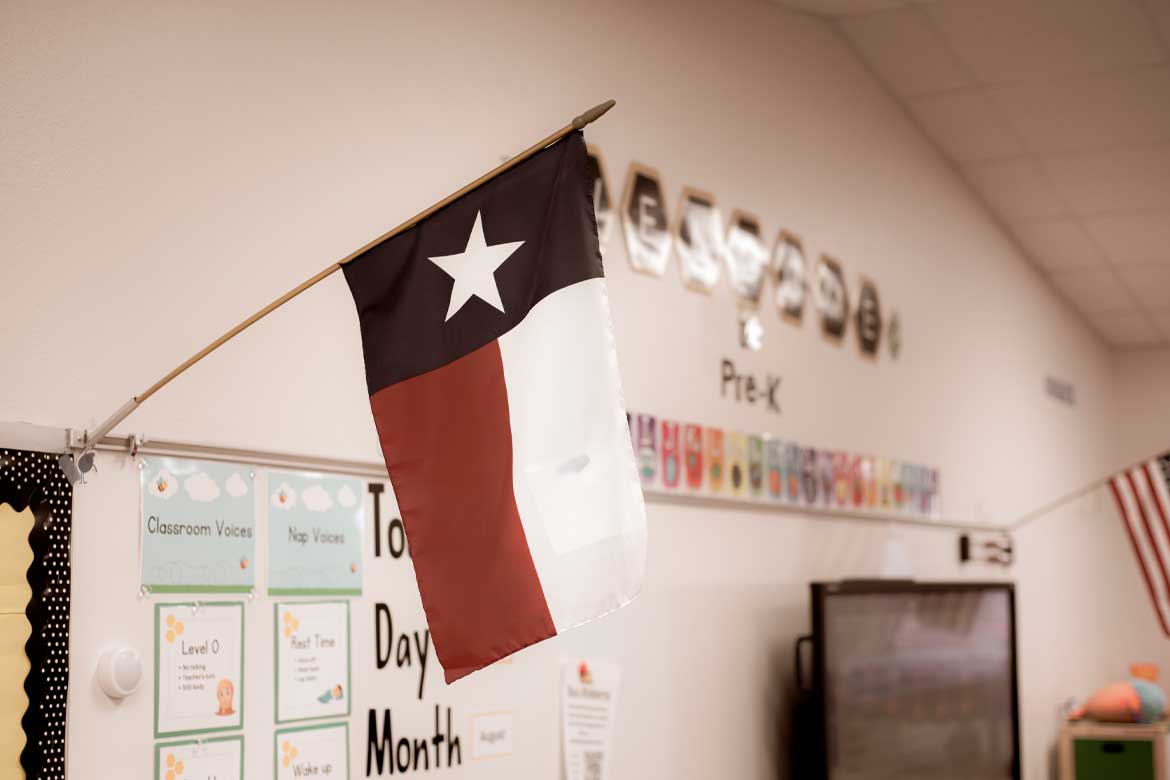 Texas and American flags proudly display in pre-kindergarten classroom near Dallas, modern preschooler class furniture, bulletin board, well organized school supply. Childhood education background