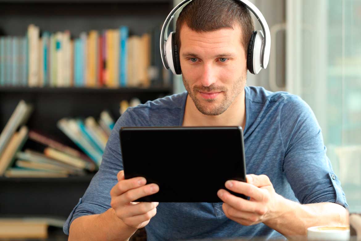 Serious man using tablet and headphones to watch online media sitting in a coffee shop