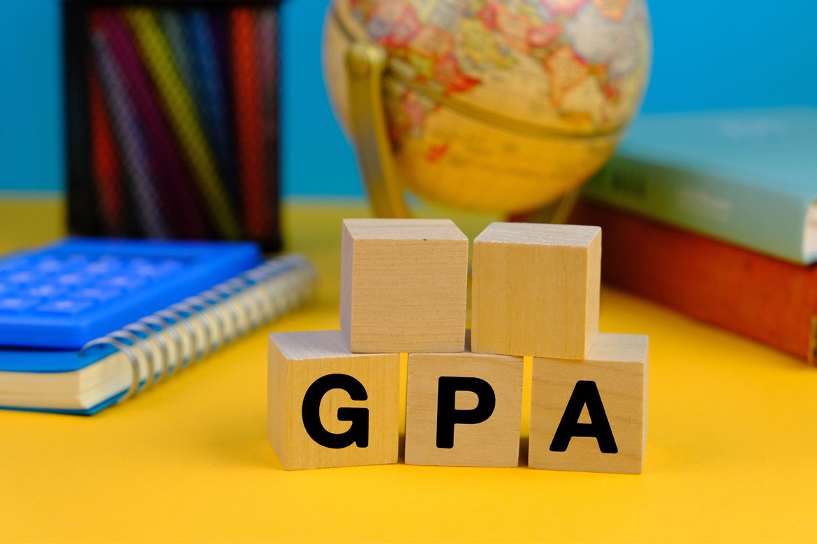 wooden block with the letters GPA or the word grade point average with the background of office tools, blue and yellow background.