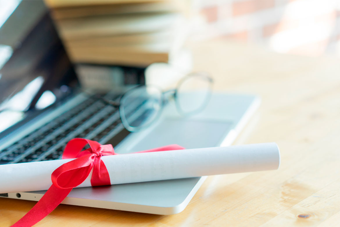 close up bachelor's degree certificate on laptop with book in the library for online learning graduation concept