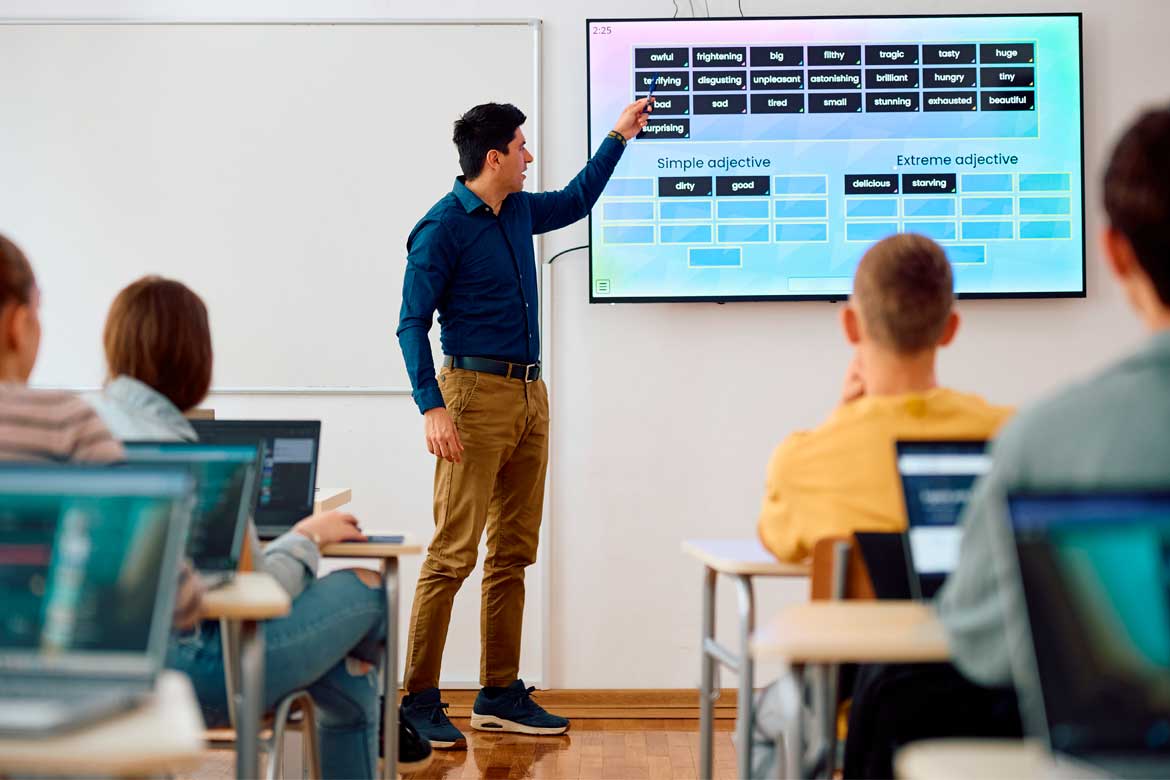 Male teacher using interactive whiteboard while giving a lesson to high school students in the classroom.