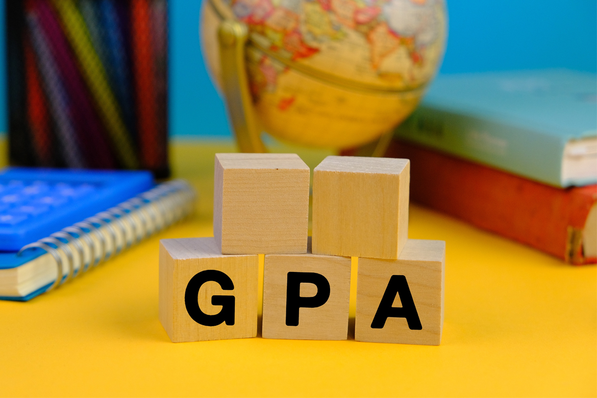 wooden block with the letters GPA or the word grade point average with the background of office tools, blue and yellow background.